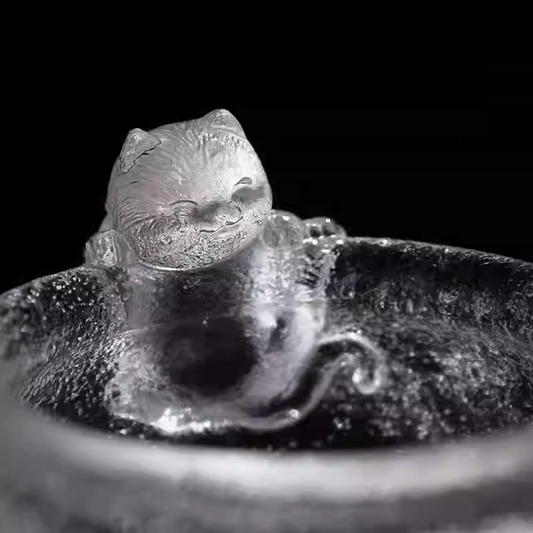 An adorable handcrafted glass teacup featuring a smiling cat sculpture on the rim, with a unique hammered ice-crackle texture.