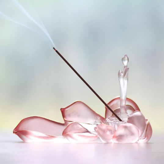 An elegant pink translucent lotus-shaped glass incense holder with wisps of smoke, captured in a bright and serene atmosphere for a mindful home ritual.