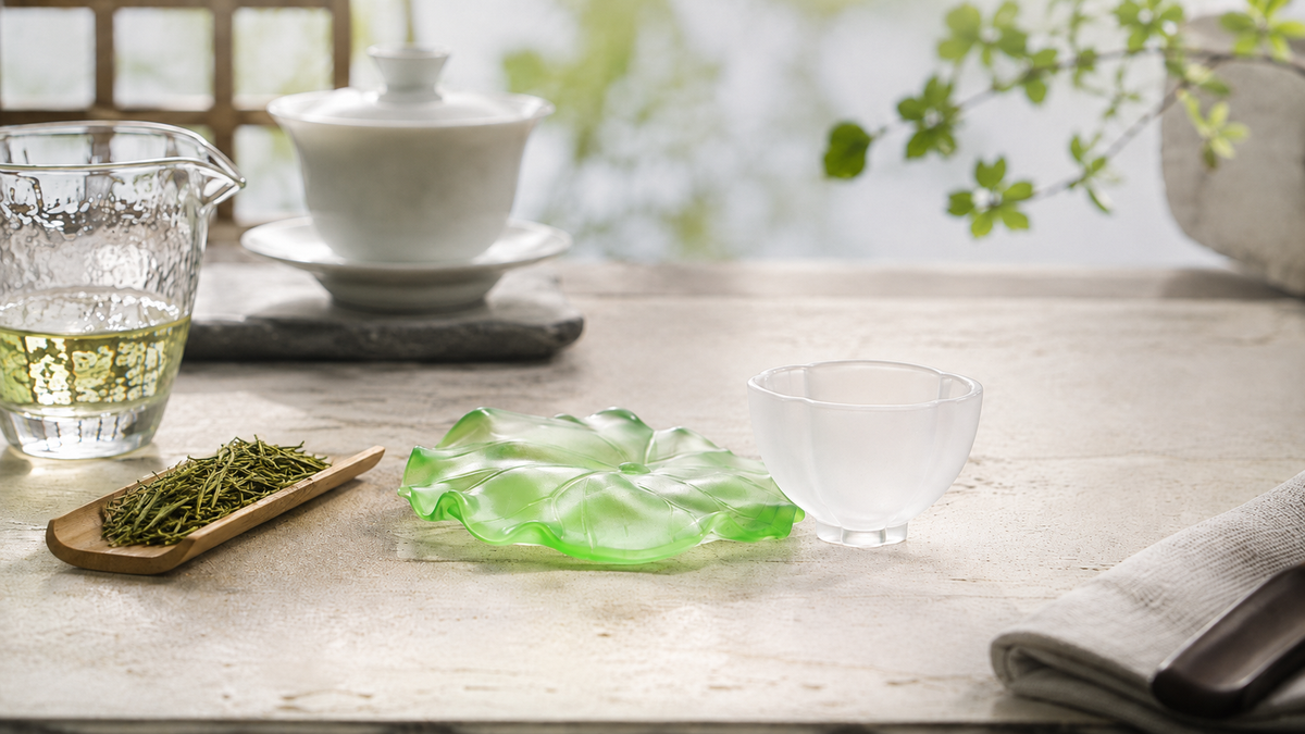 Handcrafted green Chinese liuli lotus leaf tea tray with a frosted white tea cup beside loose leaf green tea in a bright tea setting.