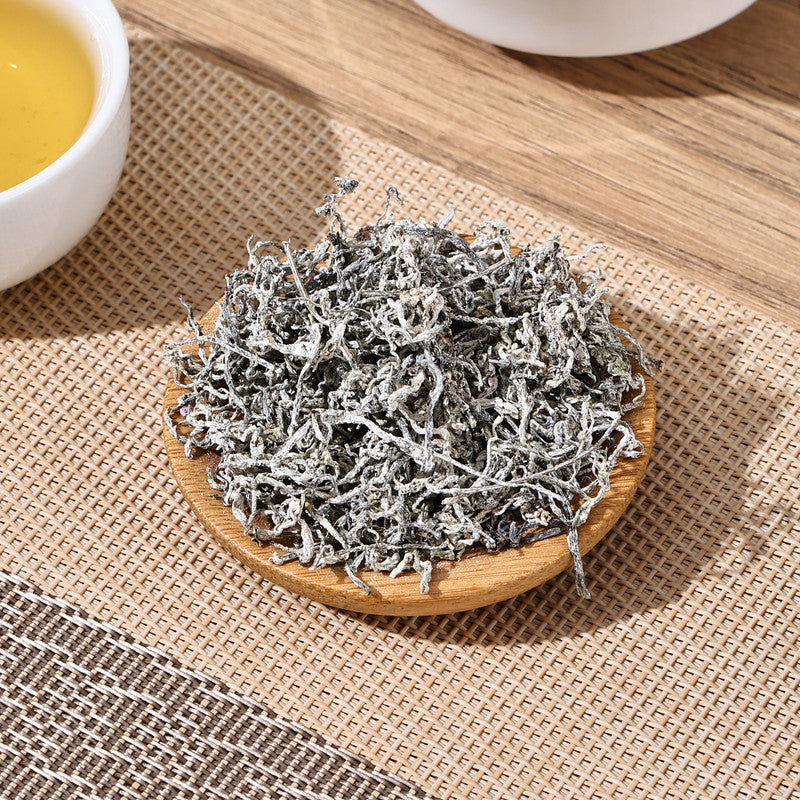 Seteng Tea loose leaf Enshi Vine Tea displayed on a wooden coaster next to a freshly brewed cup of golden herbal tea.