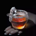 A handcrafted cat-themed glass teacup glowing with amber-colored tea, highlighting the playful kitty sculpture and sparkling hammered texture.