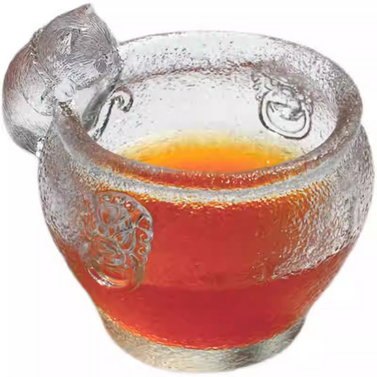 A premium handcrafted glass teacup with a playful cat figurine, featuring a sparkling hammered texture and traditional relief patterns on a clean white background.