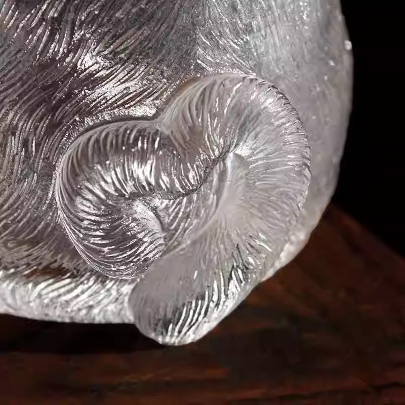 Macro close-up of a handcrafted glass teacup showing the intricate fur-like texture and a cute curled cat tail detail.