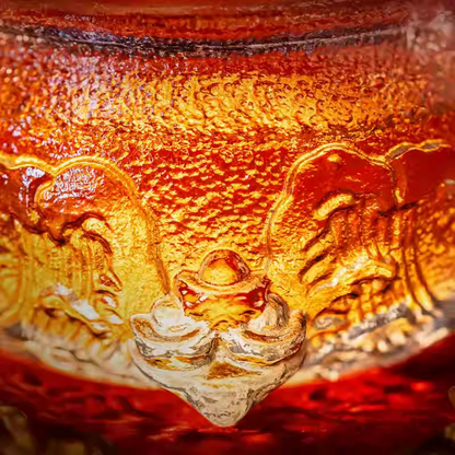 A stunning macro shot of a glass teacup featuring intricate traditional oriental relief patterns, glowing brilliantly with golden tea.