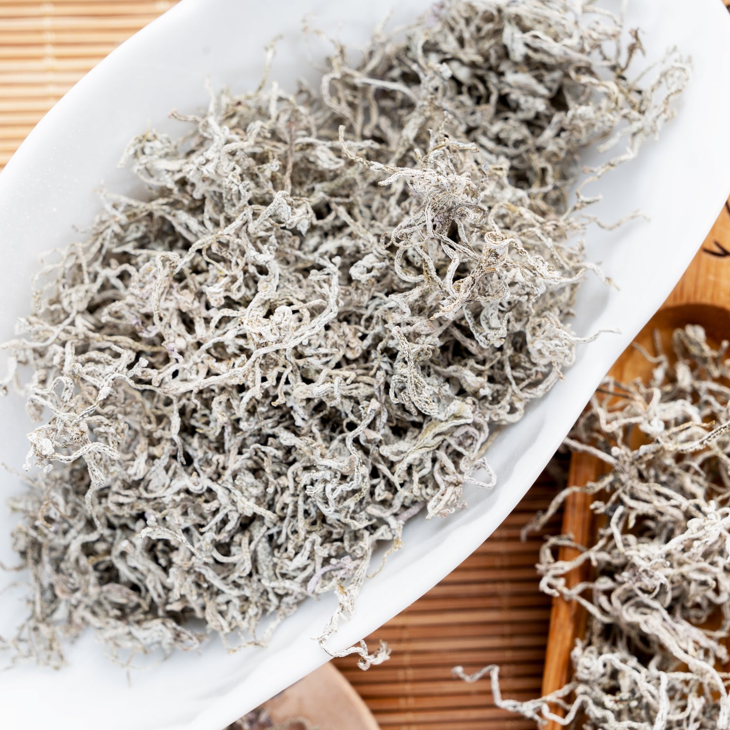 Premium Enshi Vine Tea loose leaves covered in natural white frost, beautifully displayed in a white ceramic tea vessel before brewing.