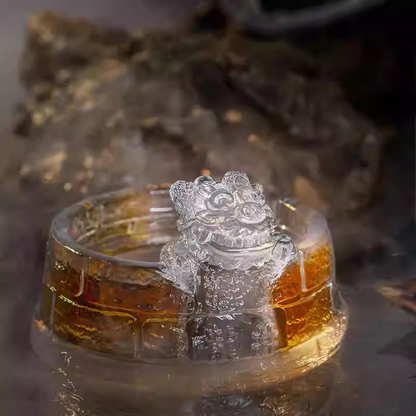 An exquisite crystal-clear glass teacup featuring a mythical guardian lion sculpture on a Great Wall textured base, glowing with golden tea.