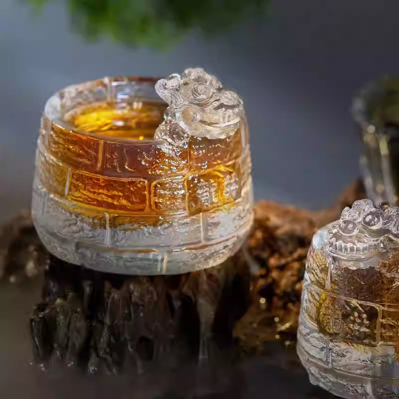 A stunning pair of crystal-clear glass teacups with guardian lion sculptures and Great Wall textures, elegantly displayed on a rustic base.