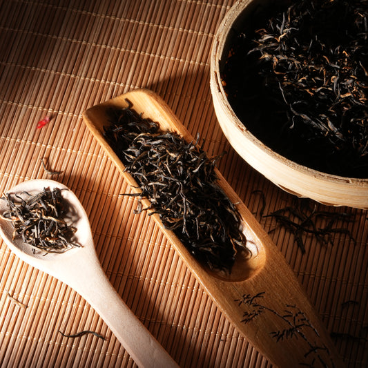 Premium Jin Jun Mei black tea leaves with distinct golden tips, elegantly displayed on a traditional bamboo tea scoop.