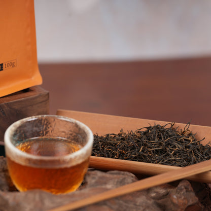 Freshly brewed Jinjunmei black tea with loose leaf tea in a wooden tray, premium Chinese black tea with rich amber color