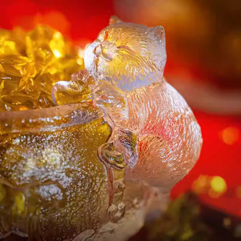Macro close-up of a handcrafted glass teacup, showcasing the exquisite fur texture of the climbing cat sculpture illuminated by golden light.