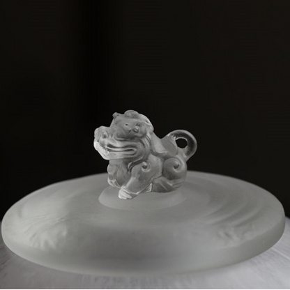 Macro close-up of an intricately sculpted guardian beast finial on a frosted glass tea caddy lid, showcasing exquisite artisanal craftsmanship.