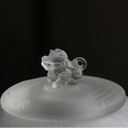 Macro close-up of an intricately sculpted guardian beast finial on a frosted glass tea caddy lid, showcasing exquisite artisanal craftsmanship.