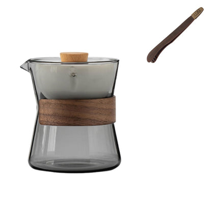 Modern minimalist tea maker featuring a smoked glass pitcher, a muted grey ceramic infuser, a walnut wood band, and matching tea tongs.
