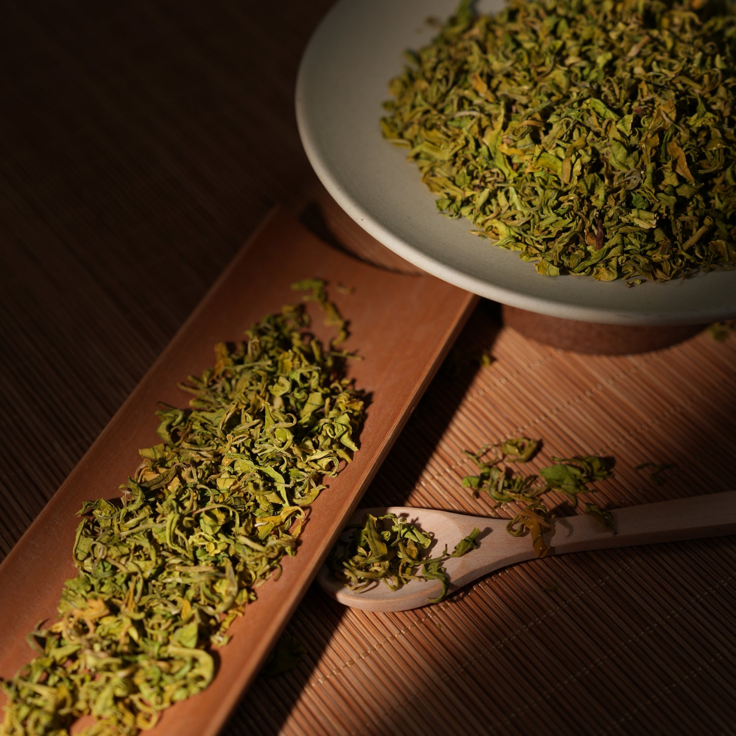 Premium SeTeng loose leaf Milk White Tea with curled, vibrant green-yellow leaves, beautifully illuminated on a traditional bamboo tea scoop under dramatic warm lighting.