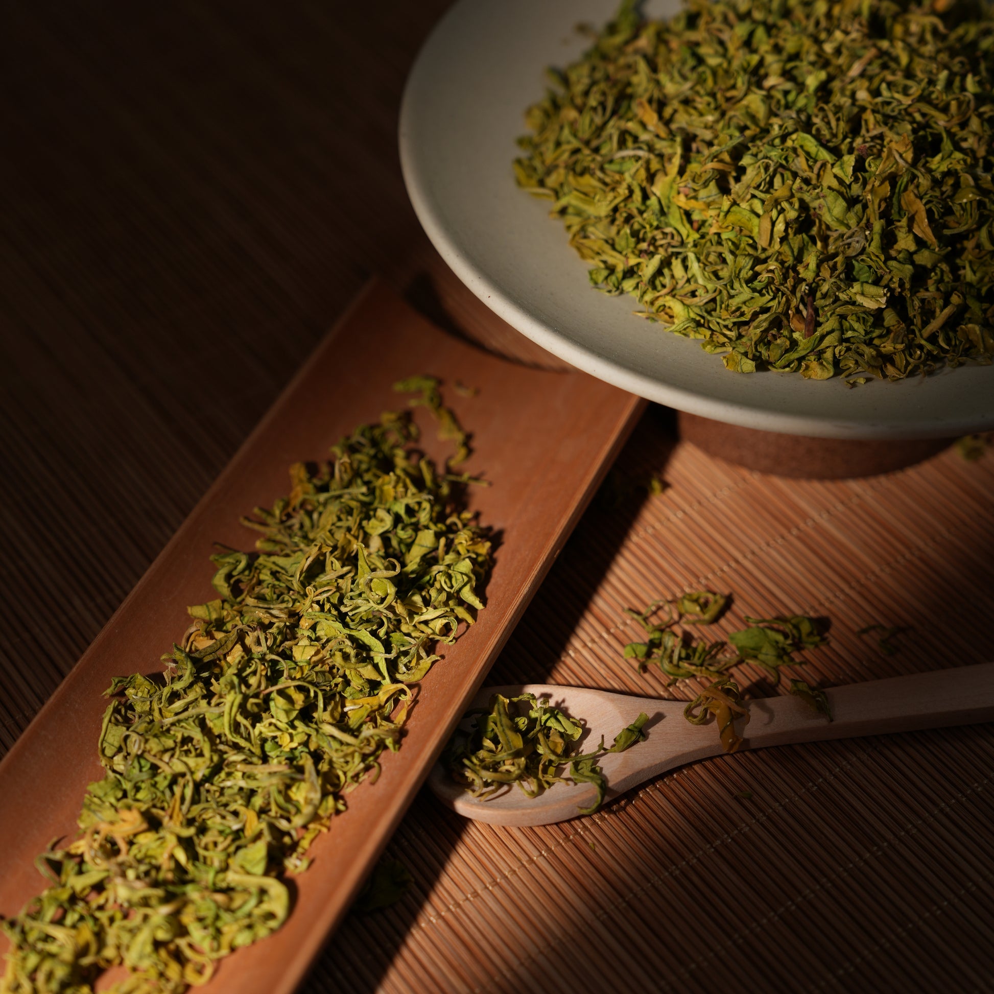 Premium SeTeng loose leaf Milk White Tea with curled, vibrant green-yellow leaves, beautifully illuminated on a traditional bamboo tea scoop under dramatic warm lighting.
