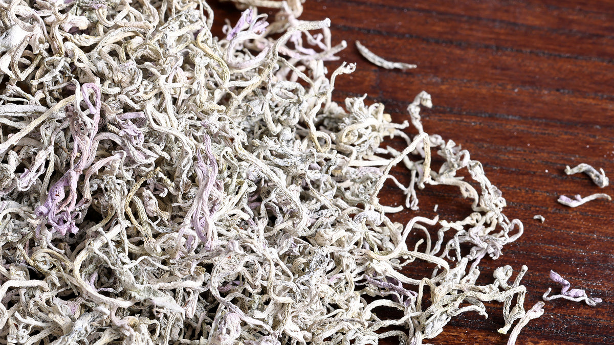 Close-up of organic Longxu vine tea with naturally white-coated curled leaves scattered on a dark wooden surface.