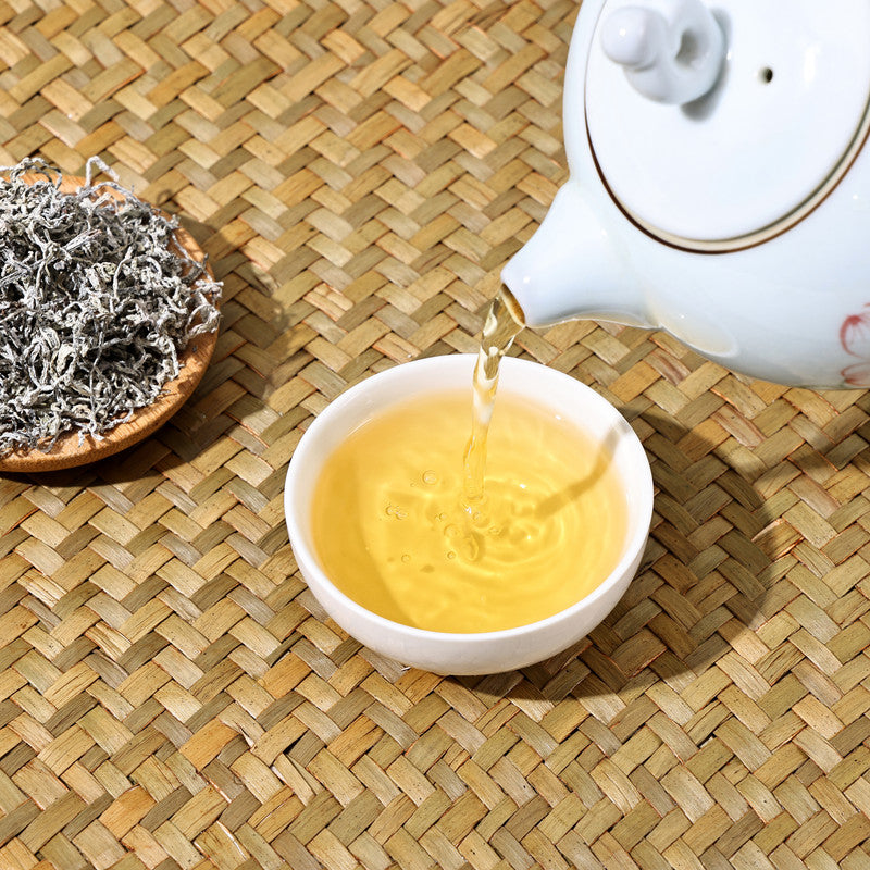 Traditional brewing of caffeine-free Teng Cha, showing the bright tea liquor and dried leaves on a woven bamboo mat.