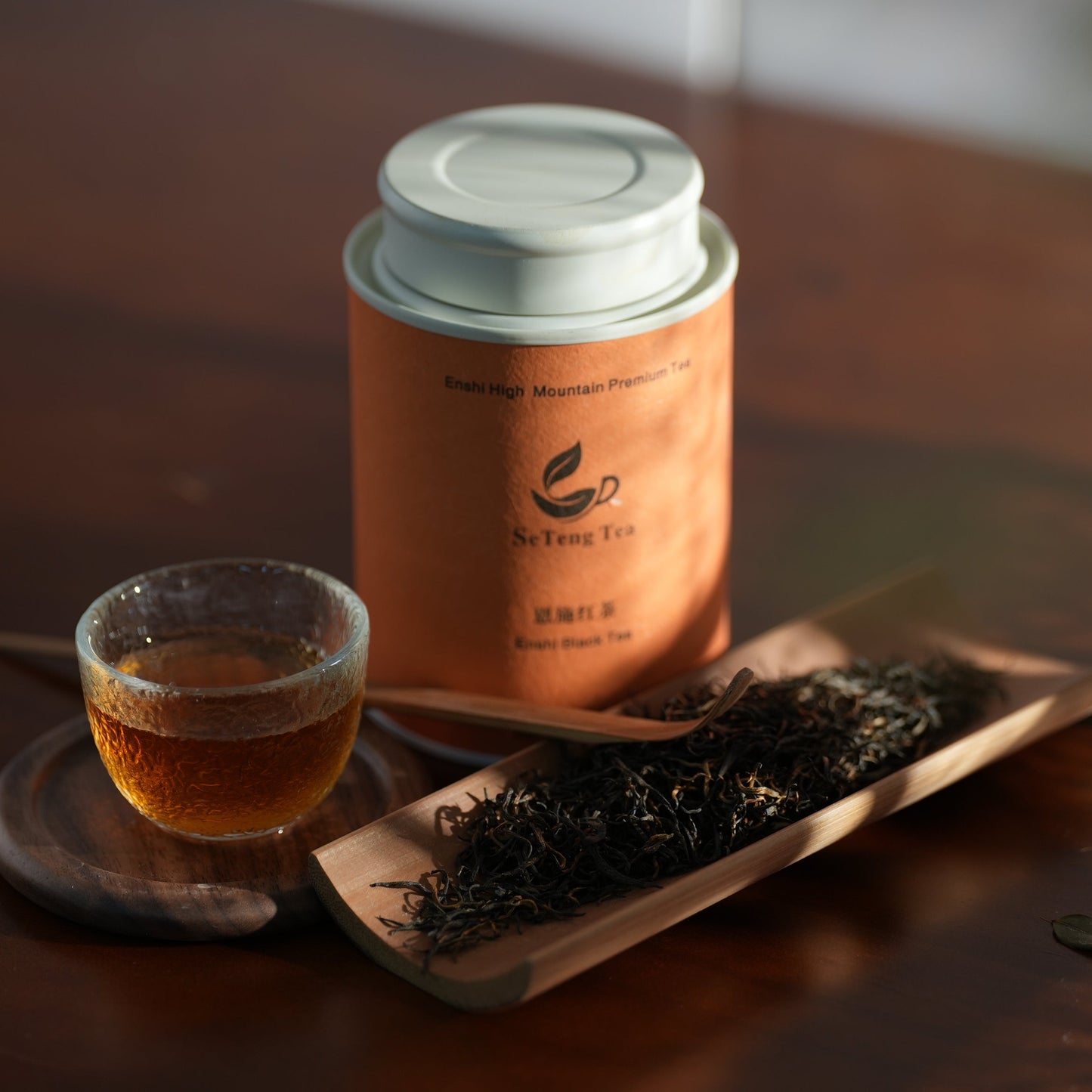 SeTeng Tea premium Enshi Black Tea canister, elegantly displayed with a glass cup of rich amber tea liquor and loose leaves on a bamboo scoop.