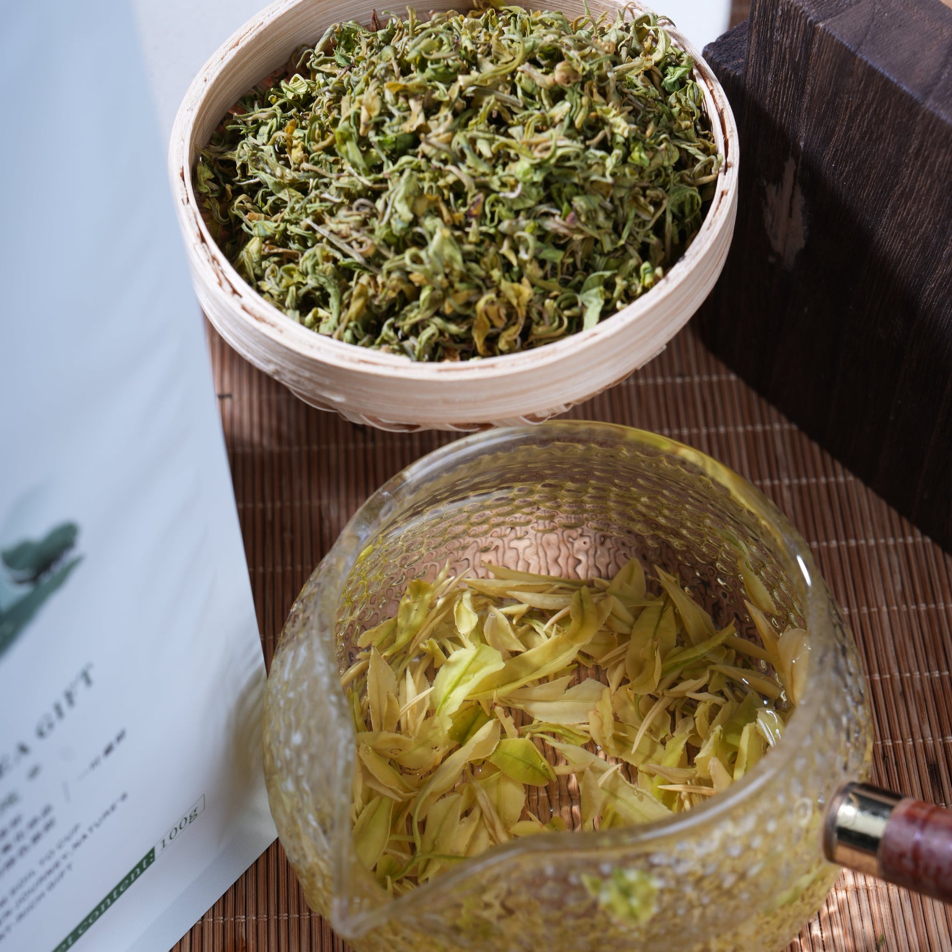 Premium SeTeng Milk White Tea showcasing curled dry leaves in a bamboo basket and beautifully expanded whole leaves steeping in a glass teapot.