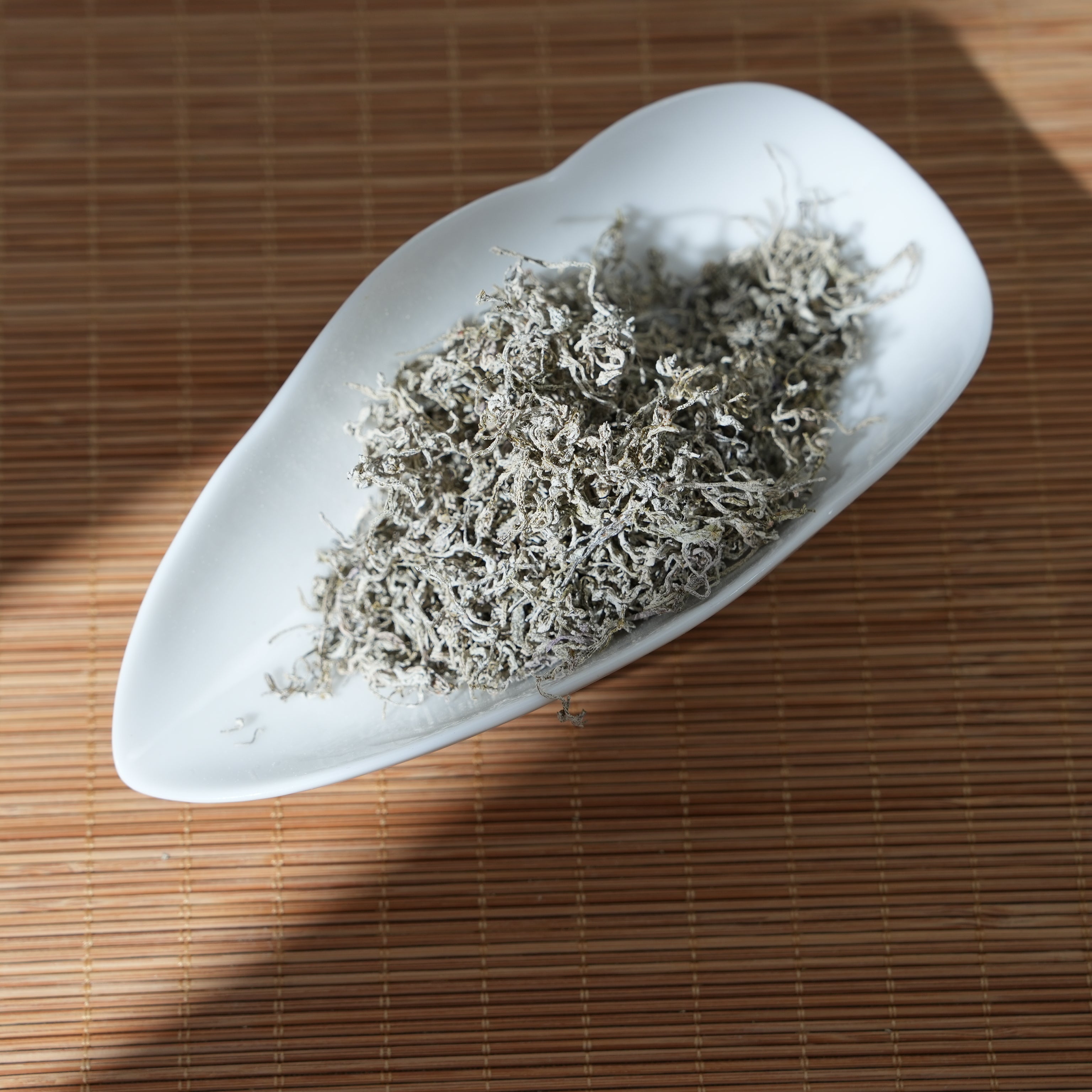 Premium Seteng Vine Tea loose leaves with natural white frost, beautifully bathed in warm sunlight on a leaf-shaped ceramic dish.